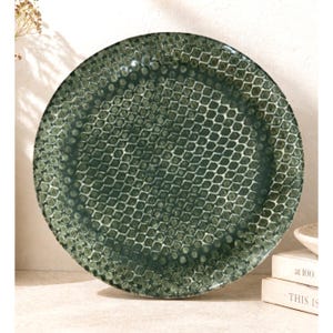 May include: A round, dark green ceramic plate with a textured, honeycomb-like pattern. The plate has a slightly raised rim and a glossy finish. The plate is a decorative piece for serving food.