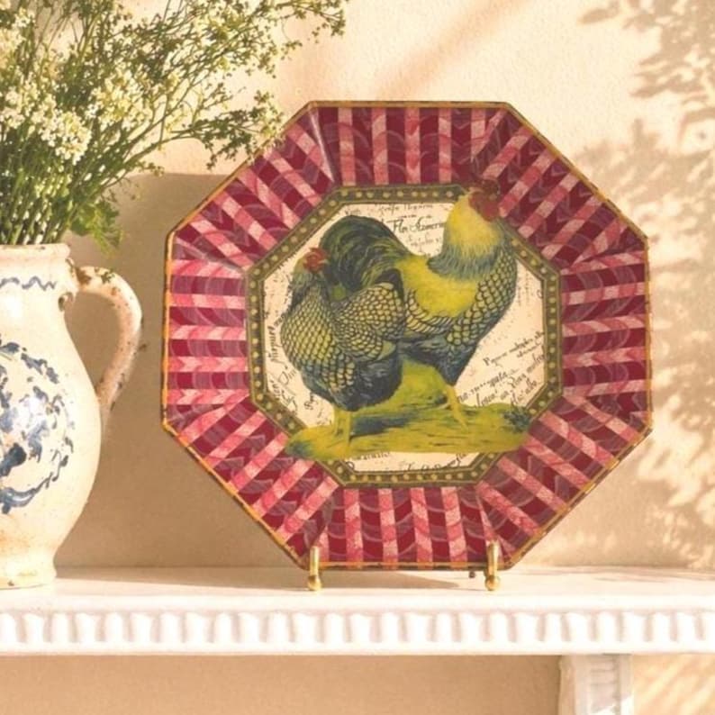 May include: An octagonal decorative plate with a rooster design. The plate features a red and white checkered border and a central image of two roosters in yellow, green, and blue. The plate is displayed on a gold-colored stand.