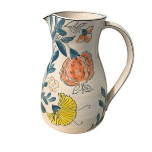 May include: Cream-colored ceramic pitcher with a curved handle and spout. The pitcher is decorated with orange, yellow, and blue floral designs. The rim and handle are outlined in black. A decorative piece for serving beverages.