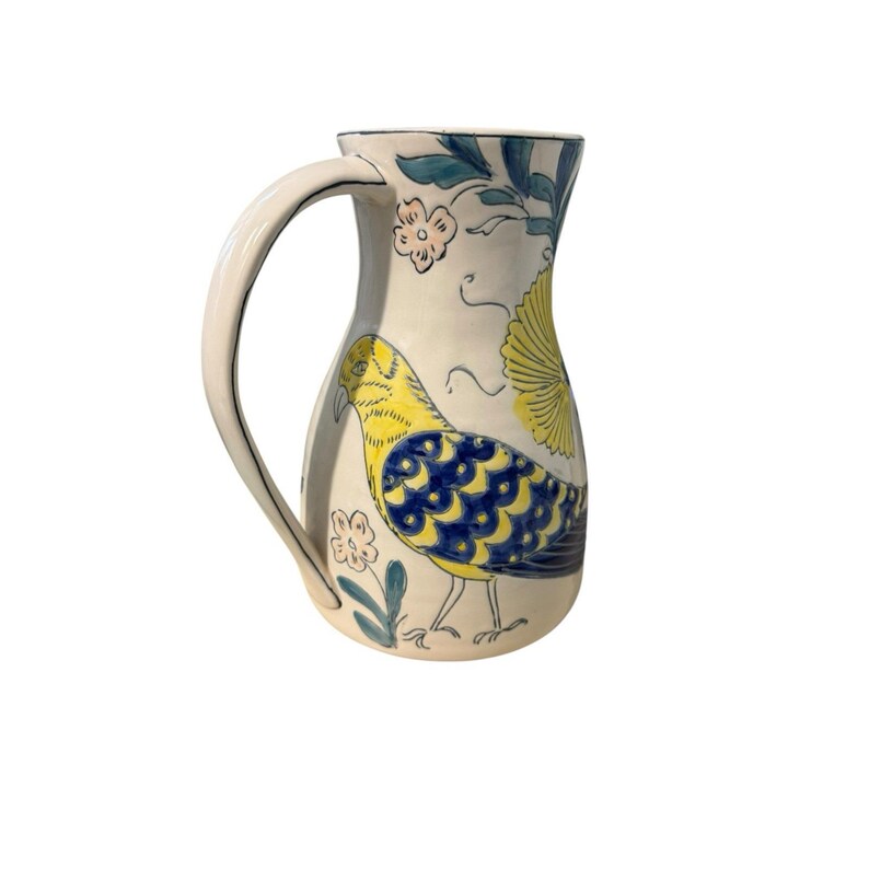 May include: Cream-colored ceramic pitcher with a large handle, adorned with a yellow and blue bird design, floral accents, and green leaves. The pitcher has a curved handle and a wide base.