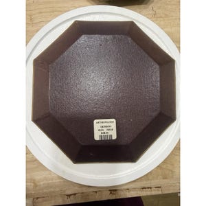 May include: An octagonal brown dish with a textured surface sits inside a white, round plate. The dish has a label with the word "ANTHROPOLOGIE" and other details. The dish is on a wooden surface.