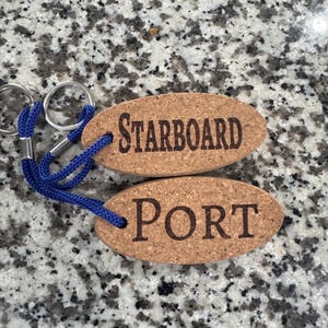 May include: Two cork keychains with blue cords and metal rings. One keychain reads "STARBOARD" in brown letters, and the other reads "PORT". The keychains are oval-shaped and made of cork.