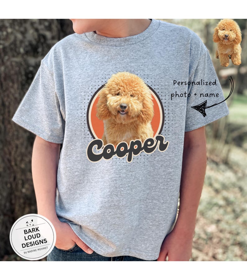 Op de afbeelding: Een grijs t-shirt met een hondenportret in een cirkel, de naam "Cooper" in een scriptlettertype. Het shirt heeft de tekst "Gepersonaliseerde foto + naam" met een pijl die naar de hondenafbeelding wijst. Een kleine hondenafbeelding staat rechtsboven.