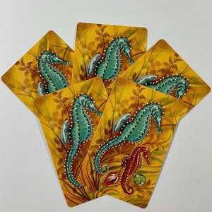 May include: A set of five rectangular cards arranged in a fan shape. Each card features a yellow background with brown seaweed illustrations and a teal seahorse. One card also displays a small red seahorse and two small shells at the bottom.