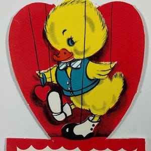 May include: A vintage Valentine's Day card featuring a yellow duck puppet with a blue vest and a red heart. The card reads "Why keep me on the string, BE MY VALENTINE".