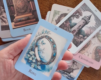 May include: A deck of oracle cards with light blue borders. One card shows a ring with blue gemstones and floral accents. Other cards depict a book, a tower, and a ship. The word "Ring" is printed on the card.