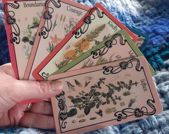 May include: A fan of five rectangular cards with rounded corners, each featuring botanical illustrations and black decorative borders. The cards display the words Boundaries, Courage, Kindly, Mercy, and Soften in a serif font, set against cream backgrounds.