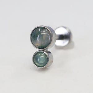 Op de afbeelding: Een zilveren oorbel met twee ronde, lichtgroene edelstenen. De edelstenen zijn gezet in een bezel setting en zijn boven elkaar geplaatst. De oorbel heeft een pin en een platte achterkant.