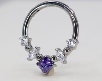 Puede incluir: Un anillo de piercing corporal plateado con una gema cuadrada púrpura y gemas redondas transparentes. El anillo está hecho de acero quirúrgico y está diseñado para un piercing de septum.