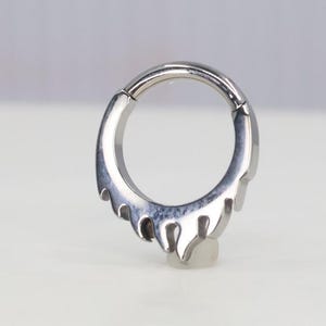 May include: A silver-colored, seamless, circular, body piercing with a drip design. The piercing is made of surgical steel.