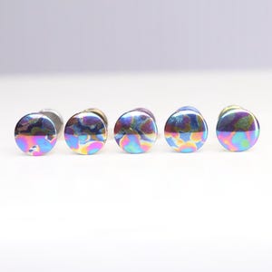 May include: Five iridescent ear gauges in different sizes, each with a circular, flat, and smooth surface. The gauges are a mix of blue, green, purple, and pink.
