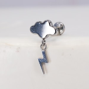 May include: Silver-toned cloud charm with a dangling lightning bolt pendant. The charm is attached to a post for a body piercing.