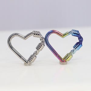May include: Two heart-shaped metal rings, one silver and one with a rainbow iridescent finish. Both rings are made of multiple connected loops.