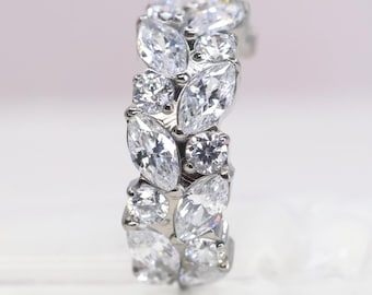 May include: A silver-toned ring featuring a cluster of clear, faceted marquise-cut and round-cut stones arranged in a dense, overlapping pattern. The band is entirely covered with these sparkling, transparent gems, creating a continuous, textured surface of brilliant white light reflections across the entire visible exterior of the jewelry piece.
