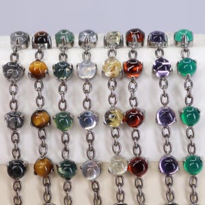 May include: Eight vertical chains made of dark metal links, each featuring a series of round, polished cabochon gemstones in various colors including black, brown, green, clear, yellow, red, purple, and bright green, set in prong settings.