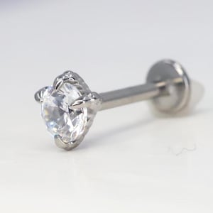 May include: A silver body jewellery piercing with a clear gemstone set in a claw setting.