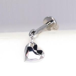 Könnte beinhalten: Ein silberner Barbell-Ohrstecker mit einem silbernen Herz-Anhänger.