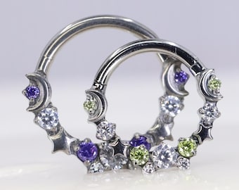 May include: Two silver-toned hinged hoop rings featuring a decorative crescent moon and star design. The rings are embellished with small, round-cut purple, lime green, and clear white gemstones set along the outer edge of the circular bands.