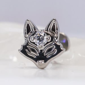 May include: A silver-colored fox-shaped earring with a clear, round gemstone set in the center. The earring has a polished finish and a post backing. The fox's features are detailed, with defined ears, eyes, and nose.