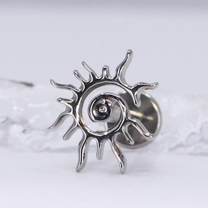 Può includere: Una spilla da bavero color argento con un design a forma di sole a spirale. La spilla presenta una spirale centrale con raggi appuntiti e radianti. La spilla è realizzata in metallo lucido e ha un perno e un retro per un fissaggio sicuro.