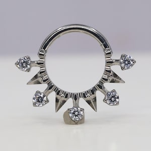 May include: Silver body jewellery with a circular ring and five pointed spikes with clear gemstones.