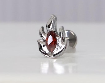 May include: A silver flame-shaped body jewelry with a red gemstone in the center. The jewelry is designed for a cartilage piercing.