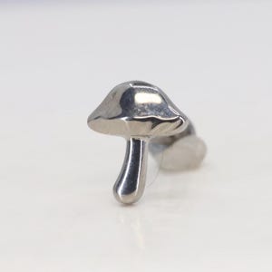 May include: A silver mushroom-shaped body jewellery piece.