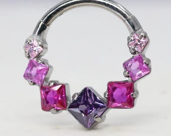 Puede incluir: Un aro de nariz plateado con una serie de piedras preciosas cuadradas multicolores. Las piedras son en tonos de rosa y morado, con una piedra central morada oscura. El anillo tiene un cierre de bisagra.