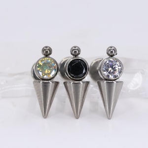 May include: Three stainless steel earrings with a cone design. Each earring has a different gemstone: one with a clear, iridescent stone, one with a black stone, and one with a clear, faceted stone.