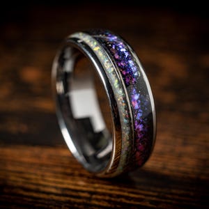 May include: A silver ring with a black band and a purple and white inlay. The inlay has a sparkly, iridescent finish.