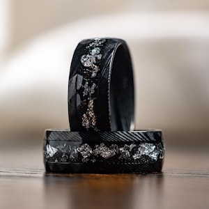 May include: Two black rings with silver and gold accents. The rings are stacked on top of each other.