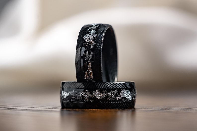 May include: Two black rings with silver and gold accents. The rings are stacked on top of each other.