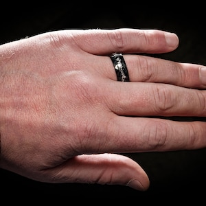 May include: A black ring with silver accents on a person's finger.