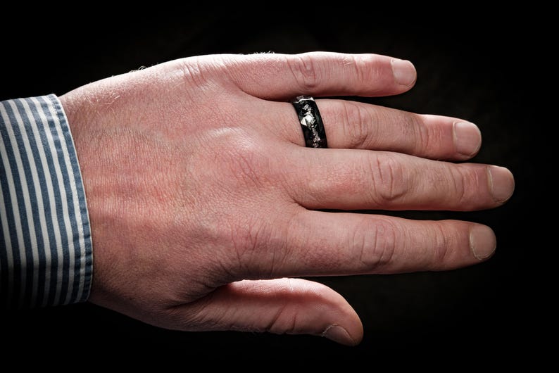 May include: A black ring with silver accents on a person's finger.