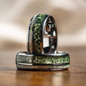 May include: Two black rings with green and white inlay. The rings are stacked on top of each other.