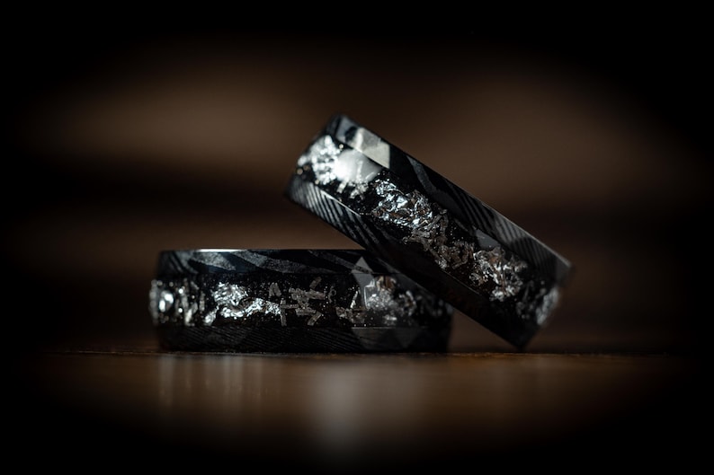 May include: Two black and silver rings with a textured finish. The rings are stacked on top of each other.