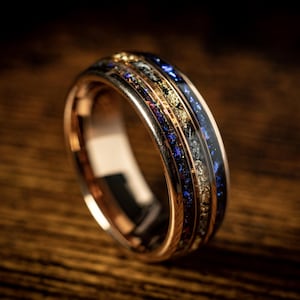 Peut inclure: Une bague en or rose avec un incrustation bleue et dorée. La bague a une finition polie et est sertie de petits diamants.