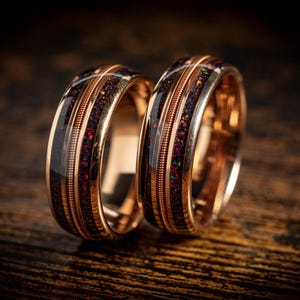 Puede incluir: Dos alianzas de oro rosa con incrustaciones negras y de cobre. Las alianzas tienen un acabado martillado y están engastadas con una fina línea de cobre.