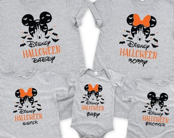 May include: A collection of grey t-shirts and a babygrow with a Halloween design. The design features a Mickey Mouse silhouette, a castle, bats, and the words "Disney Halloween" and family member names in orange.