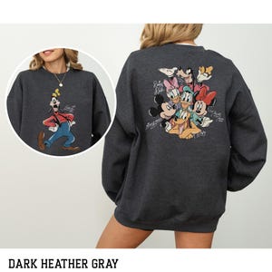 May include: Dark heather gray sweatshirt featuring a colorful graphic of Disney characters on the back, including Mickey Mouse, Minnie Mouse, Donald Duck, and Goofy. The front shows a circular image of Goofy. The sweatshirt is a crew neck style.