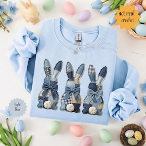 May include: Pale blue sweatshirt with three denim patchwork bunny designs, each with a bow and floral details. The text "not real crochet" is in a yellow starburst. The text "light blue" is in a blue starburst.