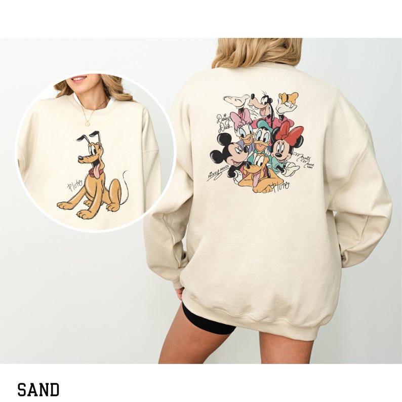 May include: Sand-colored sweatshirt featuring a Pluto graphic on the front and a group of Disney characters on the back. The Pluto graphic shows the dog in a seated position. The back of the sweatshirt features Mickey Mouse, Minnie Mouse, Donald Duck, Daisy Duck, Goofy, and Pluto.