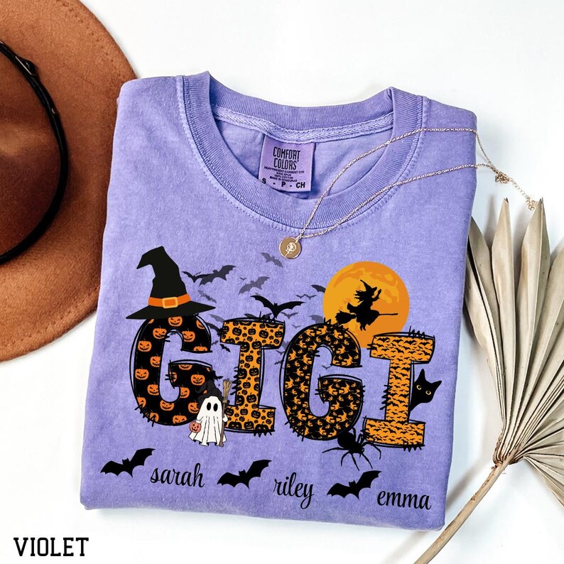 May include: A violet Comfort Colors t-shirt with a Halloween-themed design. The word "GIGI" is displayed in a combination of orange pumpkin and leopard print patterns. The shirt features bats, a witch on a broom, a ghost, a black cat, and the names "sarah", "riley", and "emma".