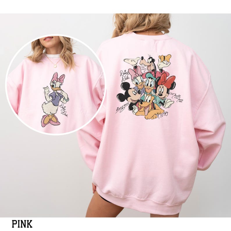May include: Pink sweatshirt featuring Daisy Duck on the front and a group of Disney characters on the back. The sweatshirt has a crew neck and long sleeves. The Disney characters include Mickey Mouse, Minnie Mouse, Donald Duck, Daisy Duck, Goofy, and Pluto.