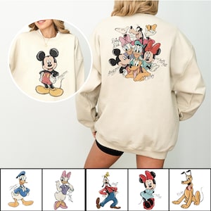 May include: Cream-colored sweatshirt featuring Mickey Mouse on the front and a group of Disney characters on the back. The front graphic shows Mickey in his classic pose. The back displays Mickey, Minnie, Donald, Daisy, Goofy, and Pluto. The sweatshirt has a relaxed fit.