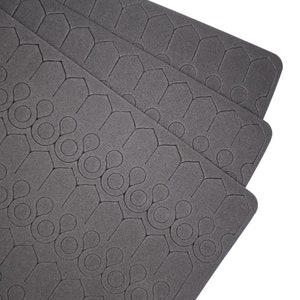 Könnte beinhalten: Drei schwarze Schaumstoffplatten mit einem sich wiederholenden Muster aus Sechsecken und Kreisen.