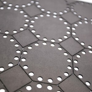 May include: A close-up of a black hexagonal patterned surface with a repeating design of circles. The surface is made of a material that appears to be leather or fabric.