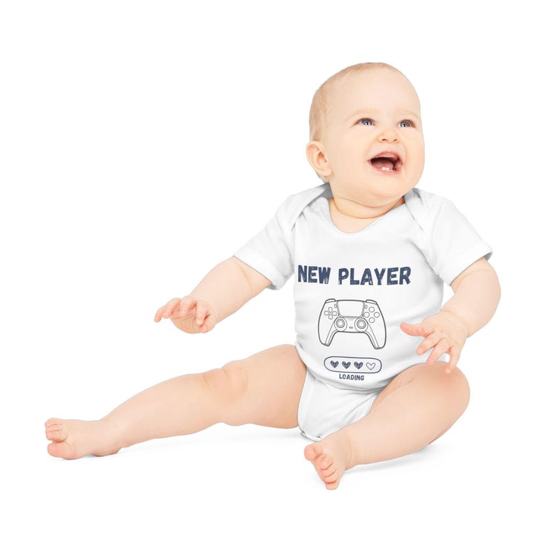 May include: A white baby onesie with a blue graphic of a video game controller and the text "NEW PLAYER" and "LOADING" with hearts.