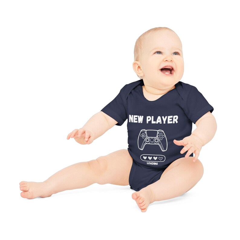 May include: A navy blue baby onesie with white text that reads "NEW PLAYER" and a graphic of a video game controller with hearts and the word "LOADING" underneath.