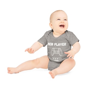 May include: A gray baby onesie with a white graphic of a video game controller and the text "NEW PLAYER LOADING".